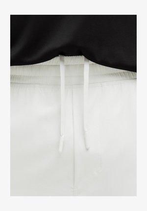 Bele trenirke z elastiko in belimi vrvicami, v kombinaciji z črnim vrhom. Gladka tekstura, športen dizajn.