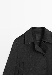 Mørkegrå uldblandingsfrakke med spids krave, dobbeltknaplukning foran, to sidelommer og sorte knapdetaljer. Ingen synlige mønstre.