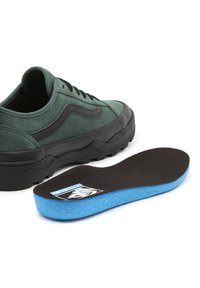 Baskets en daim vert avec des accents noirs, semelle noire épaisse et semelle intérieure amovible avec un dessous bleu et un motif texturé.