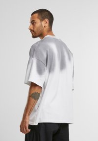 Grå og hvit tie-dye oversized t-skjorte med rund hals, korte ermer og en glatt tekstur. Har et tydelig gradientmønster.