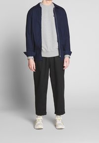 Camisa azul de botones, sudadera gris, pantalones negros y zapatillas grises con acentos amarillos. Materiales de algodón con un acabado texturizado.