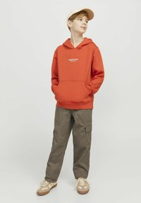 Orange hoodie med frontficka och vit textlogotyp, ihop med olivgröna cargobyxor och beige sneakers. Utseendet är avslappnat och bekvämt.