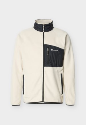 Kremowa polarowa kurtka z czarnym kołnierzem na zamek, zamkiem błyskawicznym z przodu, czarną kieszenią na piersi zapinaną na zamek oraz bocznymi kieszeniami, z logo marki Columbia.