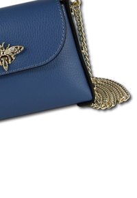 Sac en bandoulière en cuir bleu avec un accent en forme d'abeille dorée, présentant une finition texturée, un rabat et une bandoulière en chaîne métallique.
