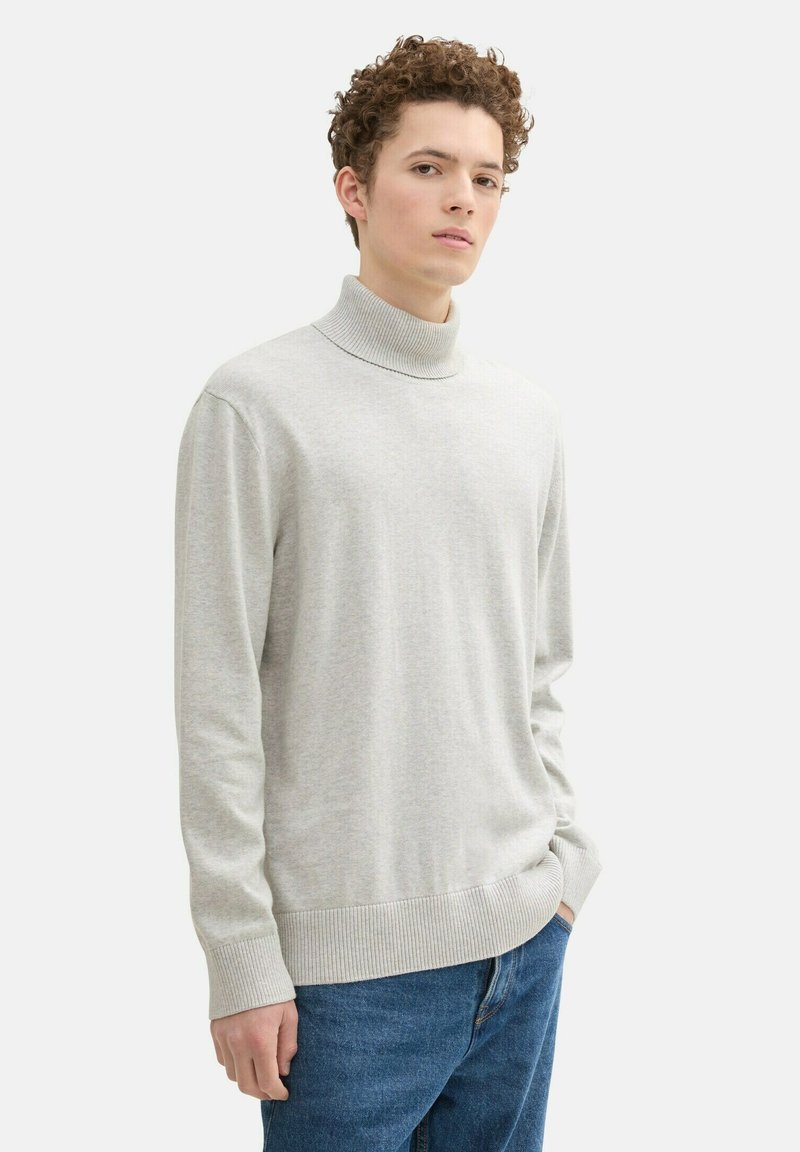 Hellgrauer Rollkragenpullover aus weichem Strickmaterial, mit geripptem Kragen und Bündchen, kombiniert mit blauen Jeans.
