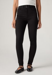 Black skinny jeans with a high waist, featuring a button closure and front pockets. Made from denim with a smooth texture.