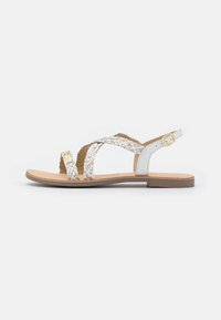 Sandale plate blanche avec des brides tressées, semelle intérieure beige et détail de boucle dorée. Présente un design minimaliste et une semelle basse.