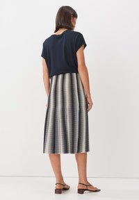 Top blu navy con maniche corte sopra una gonna midi a righe bianche e nere. Silhouette ad A con texture morbida e sandali con tacco basso.