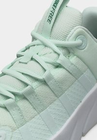 Αθλητικό παπούτσι από ανοιχτό πράσινο δίχτυ με επενδυμένη γλώσσα και περιμετρικό πλαϊνό μαξιλαράκι, με κορδόνια στο ίδιο χρώμα που περνάνε μέσα από υφασμάτινες θηλιές και λευκή σόλα.