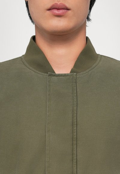 Olivgrön fleecejacka med hög krage, med en ren frontdesign, tonalt sydd och en slät yta.