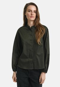 Camicia verde scuro con bottoni, maniche lunghe e colletto alla coreana. Presenta una texture liscia e elegante e polsini elasticizzati.
