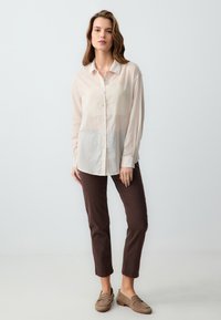 Lichtbeige knoopshirt met lange mouwen, gecombineerd met bruin aansluitende broek. De textuur lijkt zacht en iets doorschijnend.