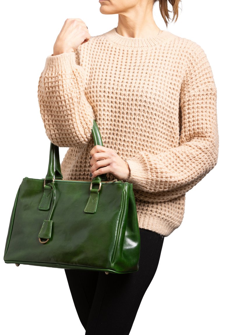 Borsa a tracolla verde in pelle con finitura lucida, doppi manici e chiusura con zip. Maglione beige testurizzato e pantaloni neri sullo sfondo.