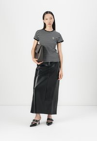 Black and white striped t-shirt in soft cotton, paired with a sleek black leather maxi skirt. Model holds a dark brown clutch and wears black heels.