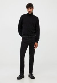 Maglione nero a collo alto, design aderente con maniche lunghe, abbinato a pantaloni neri slim-fit e scarpe nere stringate, tutto con una texture liscia.