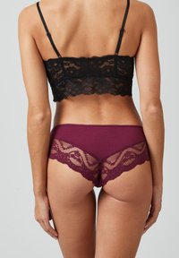 Zwarte kant bralette met verstelbare bandjes, gecombineerd met burgundy string met kantafwerking en een zacht stoffen lichaam.
