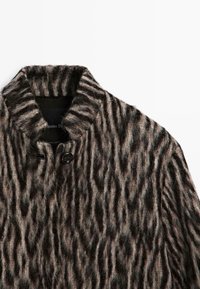 Fuzzy, geruit jasje in bruin en zwart tinten, met een opstaande kraag en een enkele knoopsluiting. Getextureerde, gestreepte stofdetails.