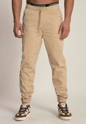 Beige Jogginghosen mit elastischem Bund und Kordelzug, mit schmal zulaufenden Beinen und Seitentaschen. Kombiniert mit braunen und weißen Sneakers.