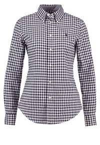 Camicia a quadri blu navy e bianca con colletto button-down e maniche lunghe. Presenta un orlo curvo e bottoni bianchi lungo la parte anteriore.