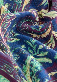 Kleurrijke stof met een bloemen- en paisleypatroon in tinten groen, blauw en bordeaux, met een gestructureerde afwerking.