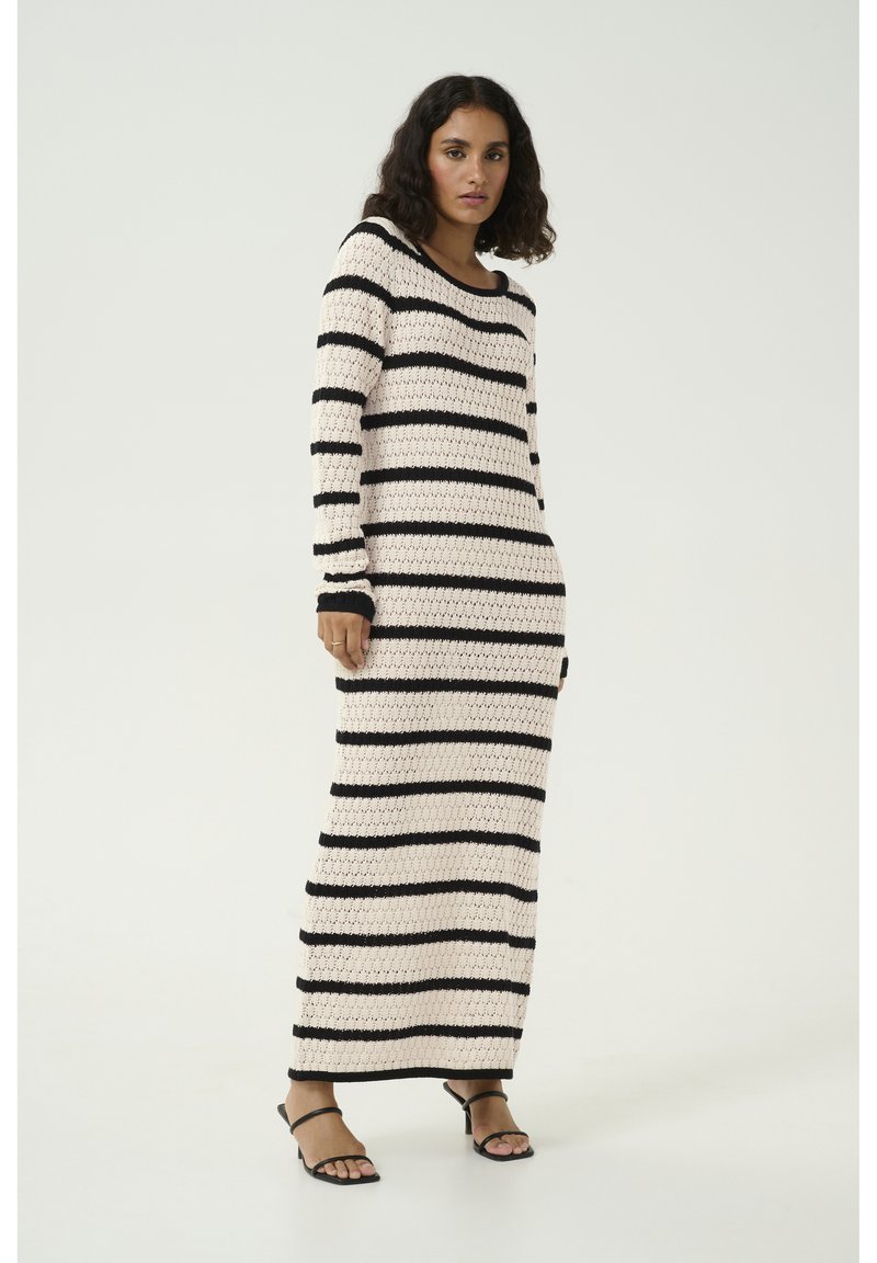 Robe maxi en tricot blanche avec de larges rayures noires horizontales, dotée de manches longues et d'un décolleté large. Texture lisse et coupe décontractée.