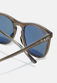 Brune plastsolbriller med blå linser, en klassisk design med dobbel bro og strukturerte armer. Ray-Ban-logoen synlig på rammen.