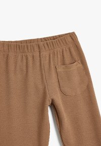 Brune, strukturerede strikbukser med elastisk talje og en enkelt baglomme med buet kant. Blød, varm og afslappet design.