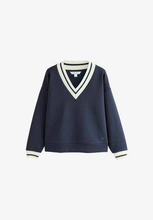 Granatowy sweter z długim rękawem oraz głębokim dekoltem w szpic z białymi i granatowymi prążkowanymi lamówkami na kołnierzu i mankietach.