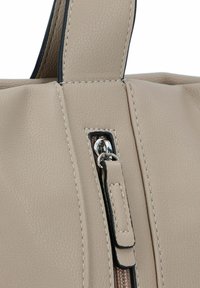 Détail d'un sac à main en cuir beige avec une fermeture éclair en métal argenté et des coutures contrastées. Le tirant de la fermeture éclair a un accent en cuir rectangulaire.