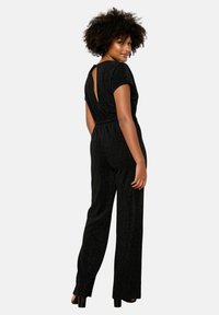 Melna, spīdīga kombinezona ar īsām piedurknēm un atslēgas formas aizmugures detaļu. Iezīmēts ar pieguļošu vidukli un platām biksēm.