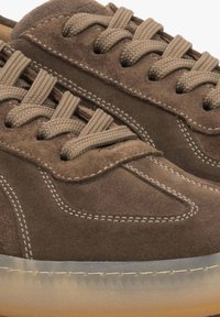 Bruine suède sneakers met een gestructureerd oppervlak, vlakke bruine veters en lichte stiksels. Transparante rubberen zool met een lichte amberkleurige tint.
