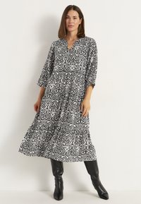 Schwarzes und weißes gemustertes Maxikleid mit 3/4-Ärmeln, einem V-Ausschnitt und Rüschendetails am Saum. Glatte Stoffoberfläche.