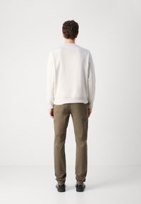 Svetlo šedý crewneck sveter, voľný strih, skombinovaný s olivovozelenými nohavicami a čiernymi topánkami; hladká textúra s rebrovanými manžetami a lemom.