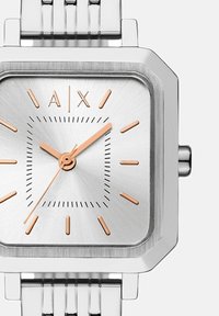 Reloj cuadrado de plata con marcadores y manecillas en rosa dorado, logo de A|X a las 12 en punto y una correa de eslabones metálicos.