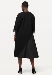 Černé šaty s tříčtvrtečními rukávy a krajkovými detaily, diagonálním lemem a saténovou podšívkou. Měkká textura, délka do poloviny lýtek.