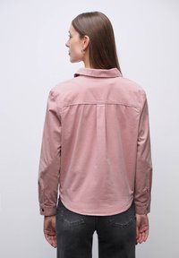 Langærmet skjorte i afdæmpet pink stof, med klassisk krave, rygfolder og knappede manchetter. Enkel og let design.