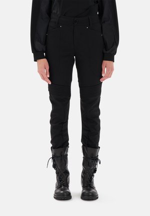 Pantaloni neri a sigaretta realizzati in materiale elastico, con dettagli a costine e tasche frontali, abbinati a stivali da combattimento neri con lacci.