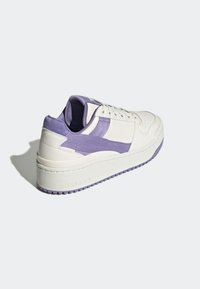 White leather sneaker with purple canvas accents, featuring a textured outsole, round toe, and lace-up front design.