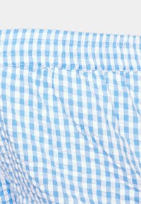 Tecido em matiz azul claro com um padrão xadrez. Apresenta uma cintura elástica franzida e um acabamento suave e texturizado.