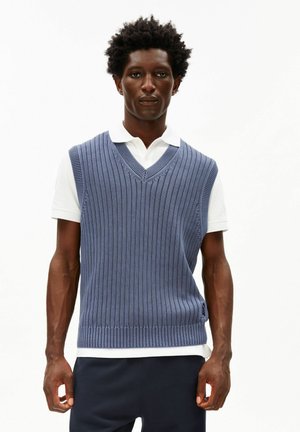 Blauw gebreid vest met verticale ribbels, V-hals, gedragen over een wit poloshirt. Heeft een losse pasvorm en zijsplitten voor comfort.