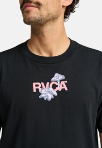 Black cotton t-shirt featuring a front graphic with "RVCA" in pink and floral designs in light blue and white. Round neck and short sleeves.