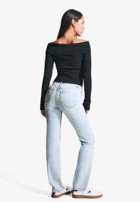 Črn rebrast top brez naramnic, svetlo modre hlače z visokim pasom in bele superge z rjavimi detajli. Model pozira od zadaj.