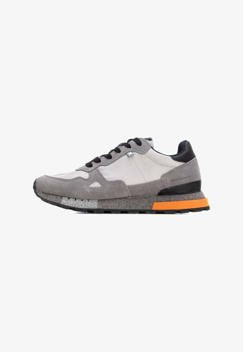 Zapatillas grises con parte superior de ante y tejido, detalles en negro, suela intermedia moteada y suela exterior naranja. Diseño de cordones con punta redondeada.