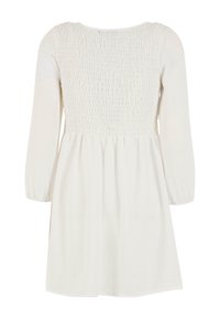 Witte jurk met een smocked lijfje, lange mouwen en een uitlopende rok. De stof heeft een zachte textuur met subtiele verticale lijnen.