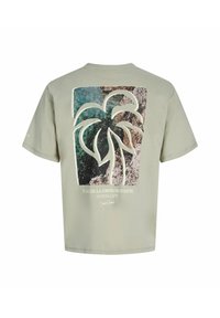 T-shirt vert clair avec un grand motif de palmier sur un fond de rochers côtiers et d'eau, avec le texte « Plage de la Corniche d'Azure ».