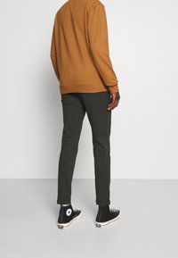 Sweatshirt marron à col rond, associé à un pantalon gris foncé coupe ajustée et des baskets montantes noires avec un logo étoile blanc.