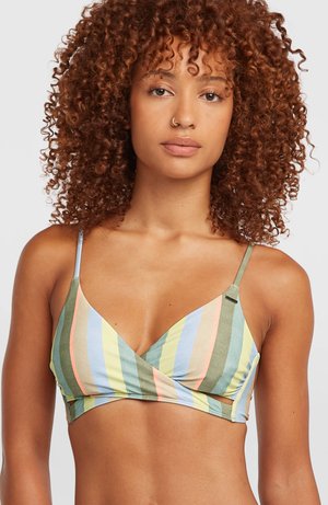 Femme aux cheveux bouclés portant un crop top rayé multicolore à fines bretelles, face à l'avant sur un fond clair uni.