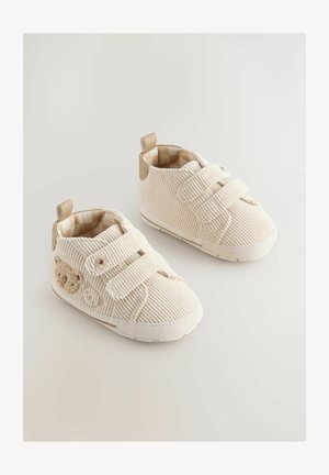 Beige kordflodskor med kardborreband, texturerad yta, vita gummisulor och ett ljust rutigt foder. Liten björn-design på sidan.