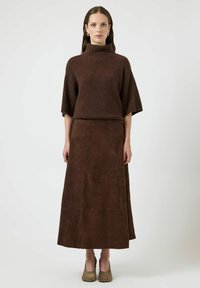 Maglione a collo alto marrone e gonna lunga in suede marrone abbinata. Entrambi i capi presentano una finitura testurizzata e una vestibilità rilassata, completati da scarpe marrone chiaro.