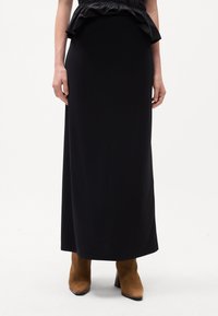 Robe maxi noire avec un corsage ajusté et un peplum froncé, texture lisse, assortie à des bottes cheville en suede beige.